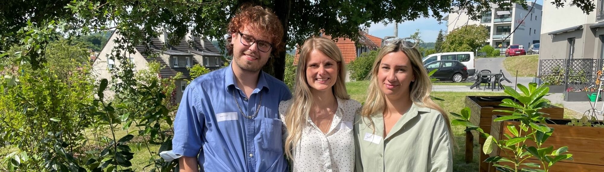 Ein junger Mann rechts und seine zwei Kolleginnen lächeln in die Kamera.