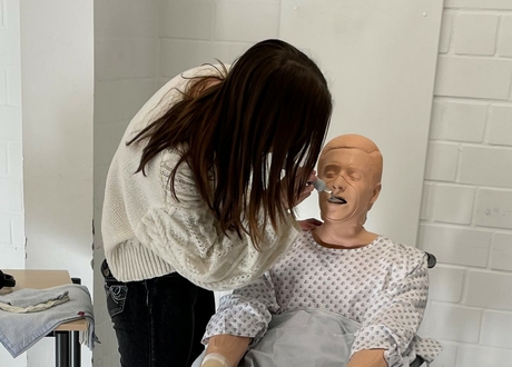 Eine Auszubildende übt Pflegetätigkeiten an einer Puppe im Rollstuhl.